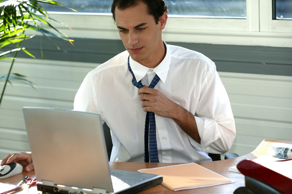 Bei großer Sommerhitze wird selbst das Sitzen im Büro zur Herausforderung Mann-im-Büro-lockert-Krawatte - Büro-Outfit im Sommer